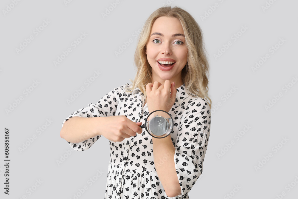 Young woman with magnifier and wristwatch on light background