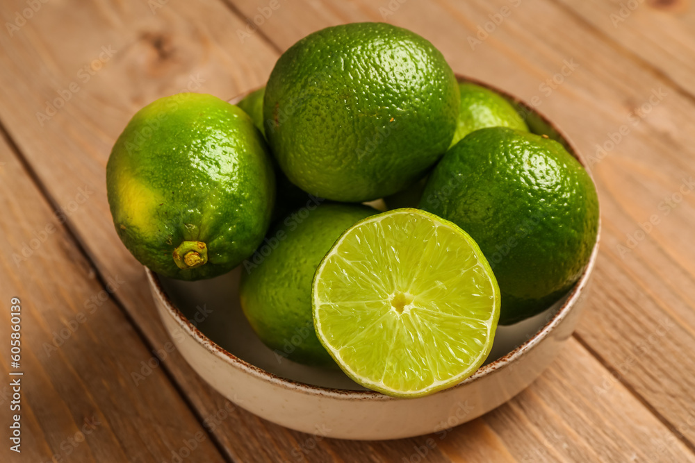 Bowl with fresh limes on wooden background