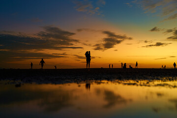 Wall Mural - Silhouettes of people walking on the ocean floor after the evening tide. Incredible colors of the evening sky