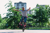 Fototapeta  - An urban oldish tattooed freestyle bike rider is doing tricks in a skate park on his bmx bike without holding handles.