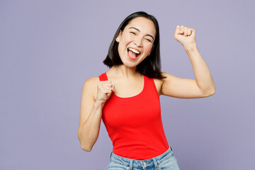 Wall Mural - Young woman of Asian ethnicity she wear casual clothes red tank shirt doing winner gesture celebrate clenching fists say yes isolated on plain pastel light purple background studio. Lifestyle concept.