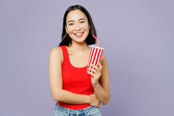 Young woman of Asian ethnicity she wear casual clothes red tank shirt hold inahnd cup of soda pop fola fizzy water isolated on plain pastel light purple background studio portrait. Lifestyle concept.