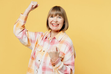 Elderly fun blonde caucasian woman 50s years old she wear casual clothes doing winner gesture celebrate clenching fists say yes isolated on plain yellow background studio portrait. Lifestyle concept.