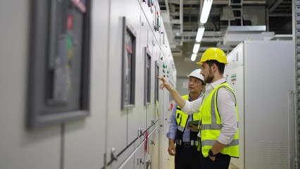 Wall Mural - Professional electrical engineer in safety uniform working at factory server electric control panel room. Industrial technician worker maintenance checking power system at manufacturing plant room.