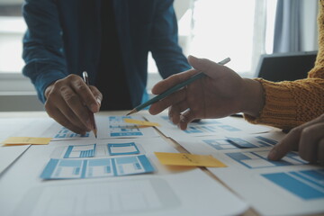 Close up ux developer and ui designer brainstorming about mobile app interface wireframe design on table with customer breif and color code at modern office.Creative digital development agency