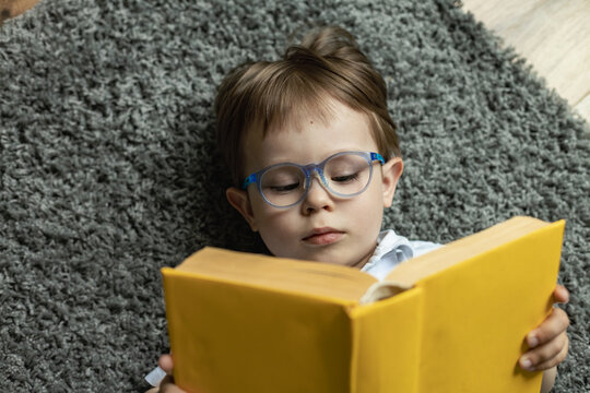 Wall Mural - little boy with glasses reading a book lying on the floor