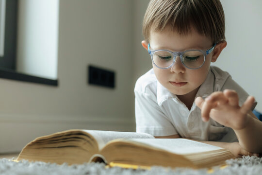 Wall Mural - smart little boy with glasses reading a book lying on the floor