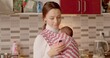 © Alena - Mother with newborn in the kitchen doing remotely, online connection by phone. Women divorced and have children or got pregnant when they didn't intend to and are raising child on their own.