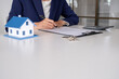 © MIND AND I - House model with real estate agent and customer discussing for contract to buy house, insurance or loan real estate background.