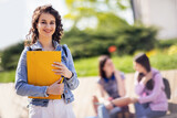 Fototapeta  - Student standing with her note-book while her friends are studying behind her