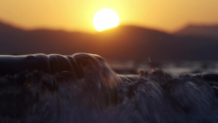 Poster - Closeup of sea waves with a blurred view of yellow sunset in the background