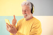 © luciano - Smiling senior man wearing headphones having video call on mobile phone. Happy elderly bearded male showing thumb up using modern technologies and wireless connection