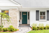 A detail of a front door on home with stone and white bricking siding, beautiful landscaping, and a colorful blue - green front door.