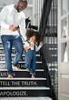 © Nassorn - Hungry baby girl holding milk bottle sucking as walking down the stairs with her father. Adorable curly hair multiracial child drinking milk. Feeding kids with dairy is essential to their growth.