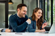 © bnenin - A smiling woman holding a credit card and sitting with a male colleague at the office.