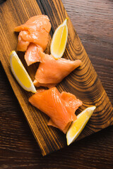 Wall Mural - Close-up of red fish, appetizing pieces of salted salmon and slices of juicy lemon on a rustic wooden board