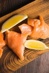 Wall Mural - Close-up of red fish, appetizing pieces of salted salmon and slices of juicy lemon on a rustic wooden board