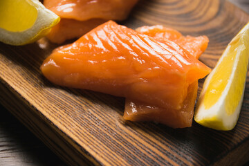 Wall Mural - Close-up of red fish, appetizing pieces of salted salmon and slices of juicy lemon on a rustic wooden board