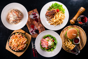 Wall Mural - Dinner set fried chicken fillet with French fries, beef burger, Italian pasta, fried potatoes with mushrooms and green salad with bacon.