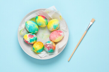 Wall Mural - Painting Easter eggs concept. Colored chicken eggs on a plate and brush, blue background