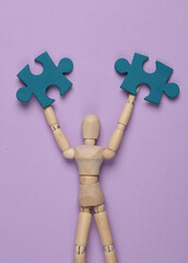 Wall Mural - Wooden puppet holding Puzzle pieces on purple background. Business concept