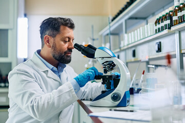 Wall Mural - male scientist analyzing test sample under microscope in lab.