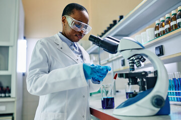 Wall Mural - black biochemist using microscope while working on scientific research in laboratory.