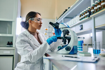female biochemist using microscope while working on scientific research in laboratory.
