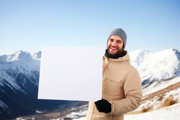 Canvas Print - Happy young man with blank board in front of him in winter mountains