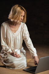 Wall Mural - Woman with coffee and laptop. Workaholism, deadline concept. Dark background. Empty room.