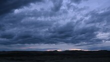 Time Lapse Of Blue Colored Evening Clouds Moving From Left To Right Above A Barren Looking Western Landscape.
