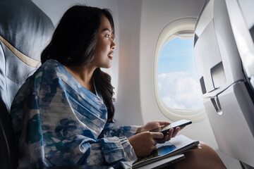 Wall Mural - A beautiful girl sits in an airplane at the window and looks at the view. Tourist travel. Happy girl at the window of an airplane.