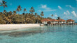 Palafitte in villaggio maldiviano con spiaggia bianca, mare cristallino, palme  e coppia di sdraio per un relax totale