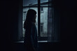 rear view of Lonely girl standing in the dark behind the window looking