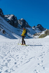 Wall Mural - view of active man ski touring at mountains background at sunny winter day. Ski mountaineer with red jacket walking up along a steep snowy ridge with the skis in the backpack