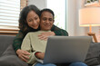 © saltdium - Middle-aged Asian woman hugging husband from behind while he was working on the sofa.