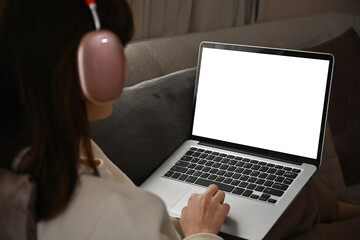 Poster - Rear view image with Asian female wearing headphones and using laptop computer while long sitting on the sofa, Empty screen of laptop.