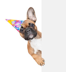 Poster - French bulldog puppy wearing party cap looks from behind empty white banner. isolated on white background
