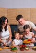 © dvulikaia - Young parents teach their little daughters to cook vegetarian salad at the kitchen.