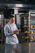 © Guys Who Shoot - a woman baker in a uniform near the shelves with freshly baked bread holds a tablet in her hands checks bread bakery