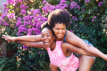 Wall Mural - Two best friends hugging piggyback outside in summer, pink flowers friendship