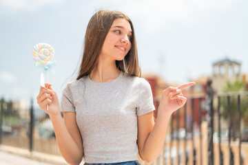 Poster - Teenager girl holding a lollipop pointing to the side to present a product