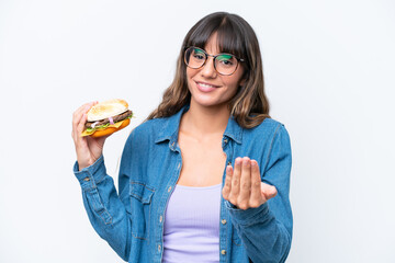 Wall Mural - Young caucasian woman holding a burger isolated on white background inviting to come with hand. Happy that you came