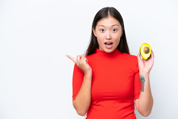 Wall Mural - Young Asian woman holding an avocado isolated on white background surprised and pointing side