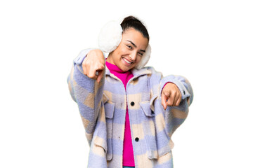 Poster - Young woman wearing winter muffs over isolated chroma key background points finger at you while smiling