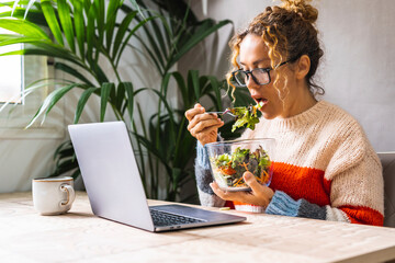 Healthy lifestyle people and business busy activity. One woman eating green fresh salads in front of a computer at the table in office or home work place. Concept of body and mental care. Diet food