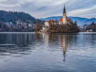 Wall Mural - Lake Bled island church and bled town in the background during a cloudy afternoon, Bled, Slovenia