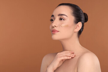 Wall Mural - Woman with swatch of foundation on face against brown background. Space for text