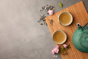 Wall Mural - Traditional ceremony. Cups of brewed tea, teapot and sakura flowers on grey table, flat lay with space for text