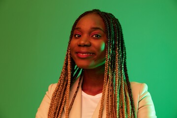 Wall Mural - African american woman portrait business smile on green background in neon light, color mixed light, bright colors. Beauty African American woman with pigtails emotions.